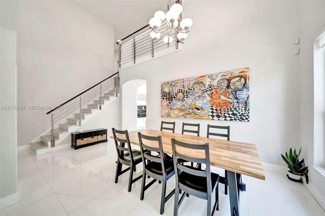 High-ceilinged room featuring large-format tile flooring, a multi-globe chandelier, and an open staircase with a metal cable railing system