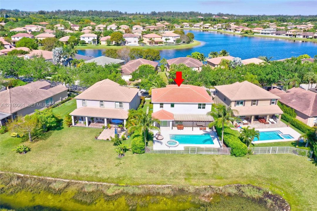 Waterfront residence featuring a two-story architectural design with a terracotta tile roof, expansive manicured lawn, mature landscaping, in-ground swimming pool with surrounding hardscaping, and direct waterfront access overlooking the lake community