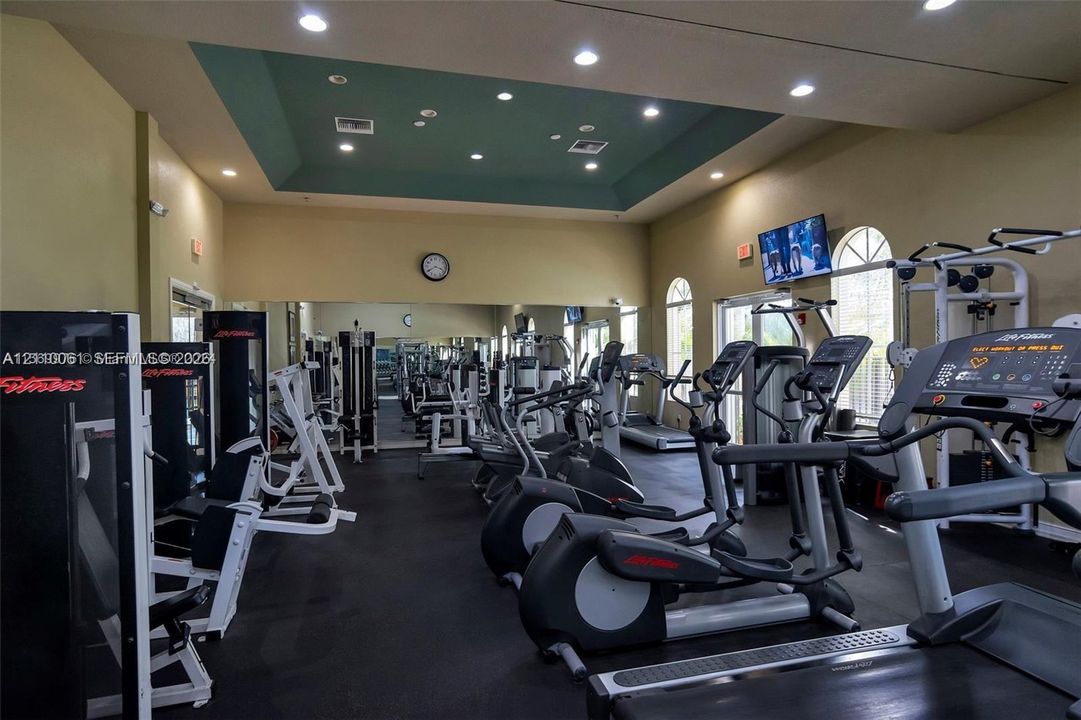 Fitness center featuring a tray ceiling with recessed lighting, wall-to-wall mirrors, and arched windows