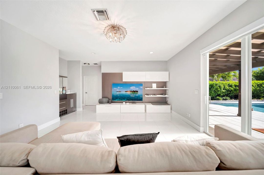 Large-format tile flooring, built-in media cabinetry with shelving, recessed lighting, and sliding glass doors leading to a covered patio with an outdoor pool
