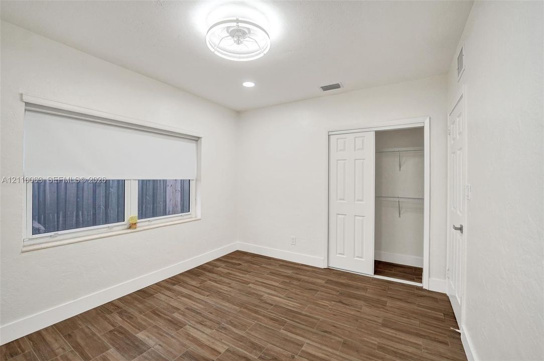 Room featuring wood-finish tile flooring, white walls, a multi-panel sliding closet door, and a circular flush-mount ceiling light fixture