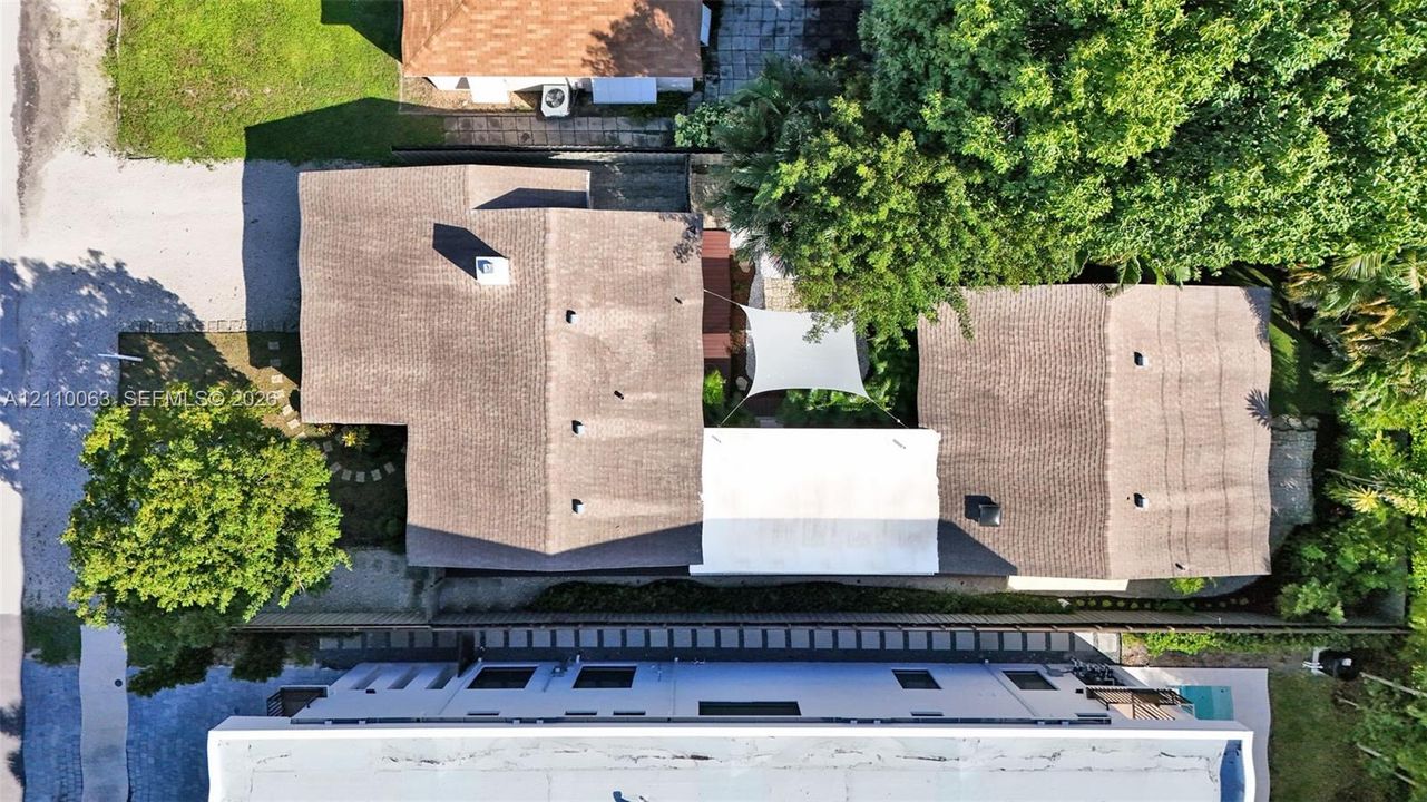 Aerial perspective of a multi-structure property featuring shingle roofing, mature trees, and a private courtyard area with a shade canopy