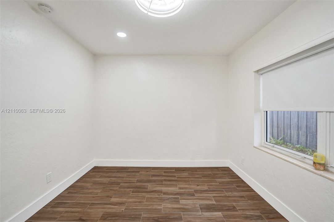 Neutral-toned room featuring wood-finish tile flooring, a recessed ceiling light fixture, and a single window with an integrated roller shade