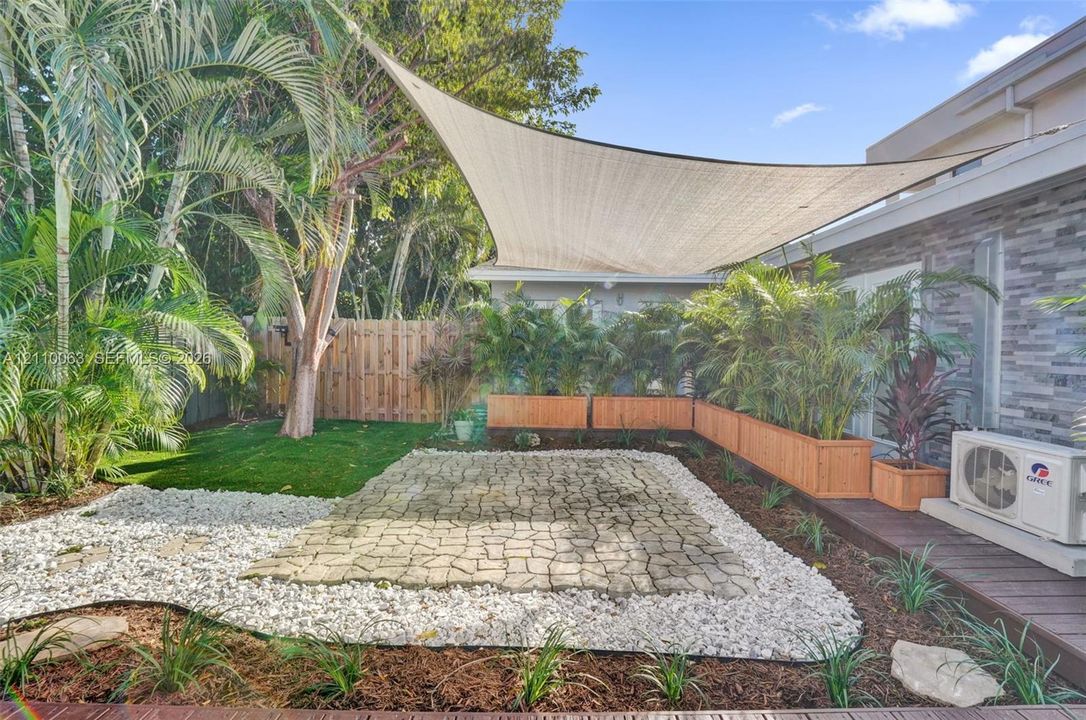 Private backyard featuring a paved stone patio, a custom overhead shade sail, integrated wood-finish planters, and a perimeter wood privacy fence