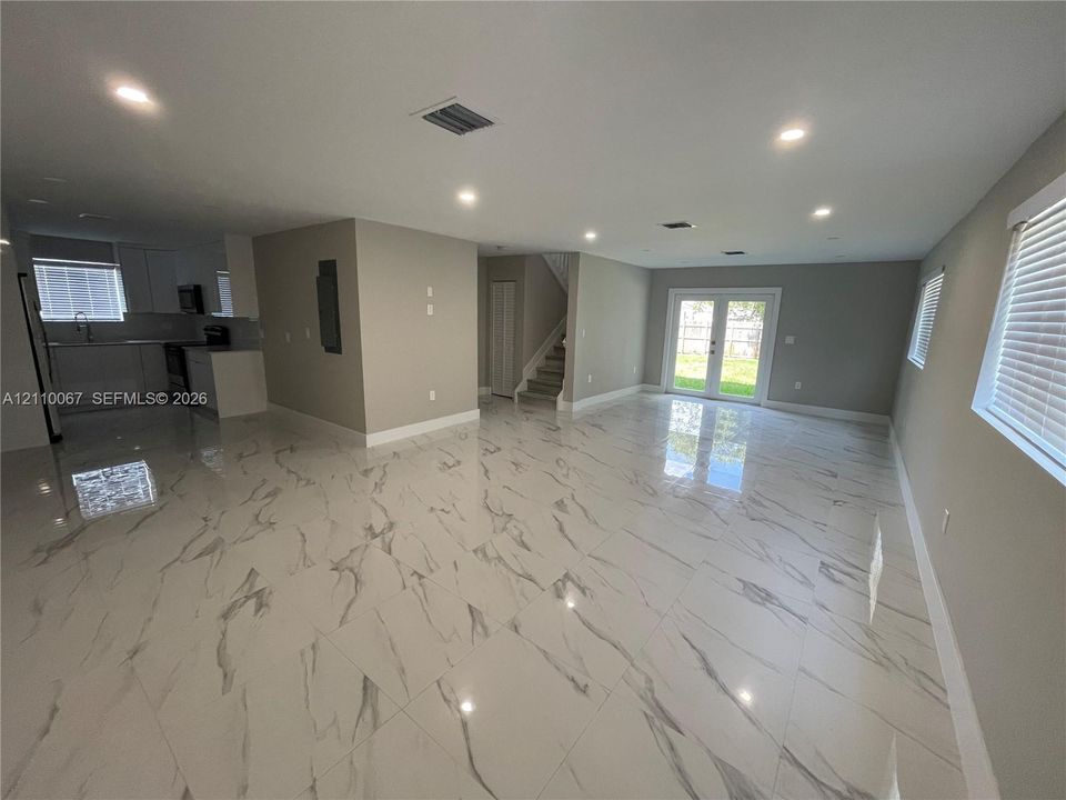 Large format, stone-finish tile flooring, recessed ceiling lighting, dual French doors providing exterior access, and a kitchen featuring built-in cabinetry