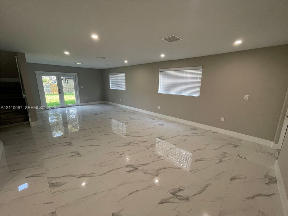 Open interior space featuring polished stone-finish flooring with veining, recessed lighting, neutral wall paint, and glass-paneled double doors
