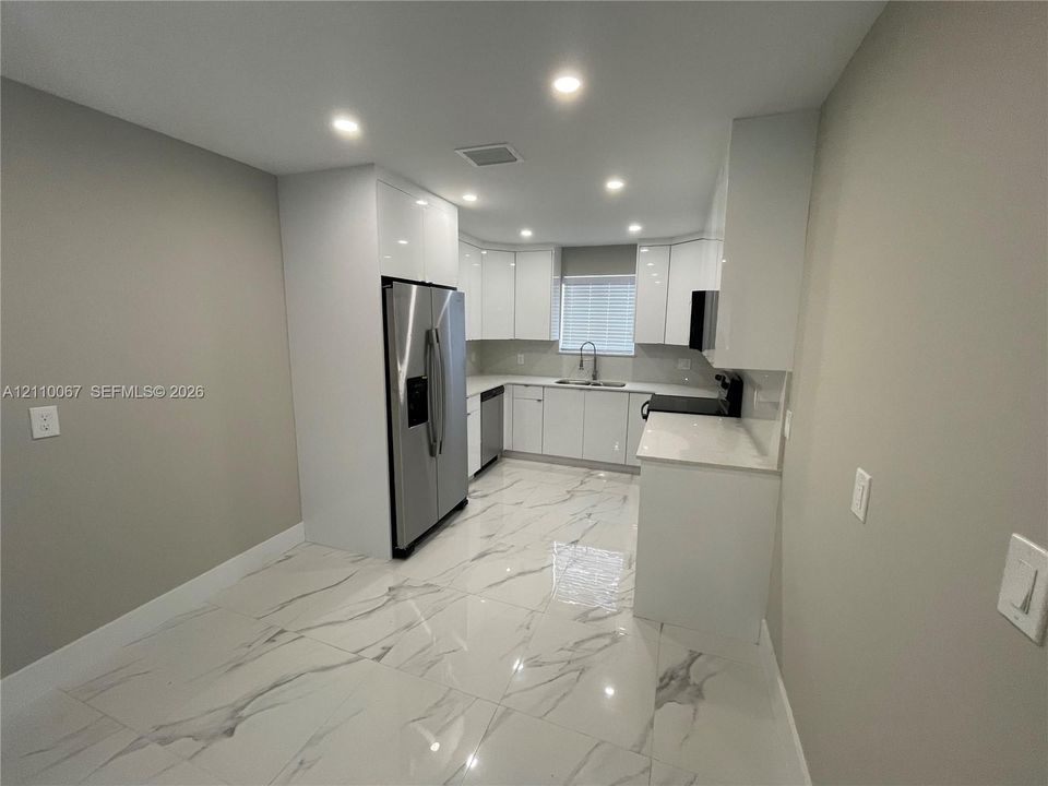 Kitchen featuring high-gloss white cabinetry, white stone-finish countertops, large-format tile flooring, stainless steel side-by-side refrigerator, and recessed ceiling lighting