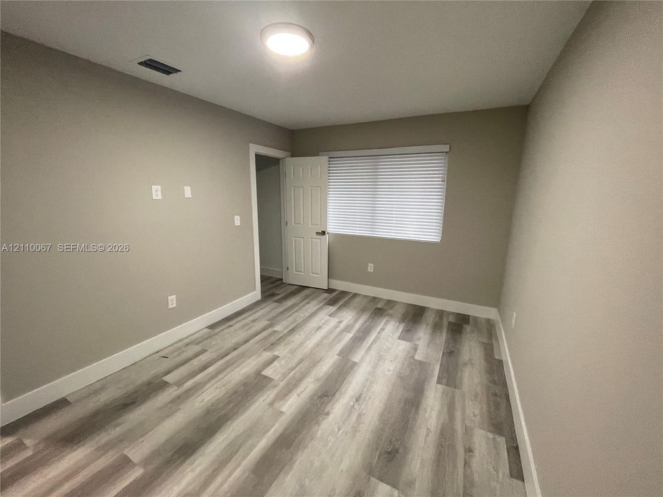 Neutral-toned walls featuring wood-finish flooring, a flush-mount ceiling light fixture, a six-panel door, and horizontal window blinds