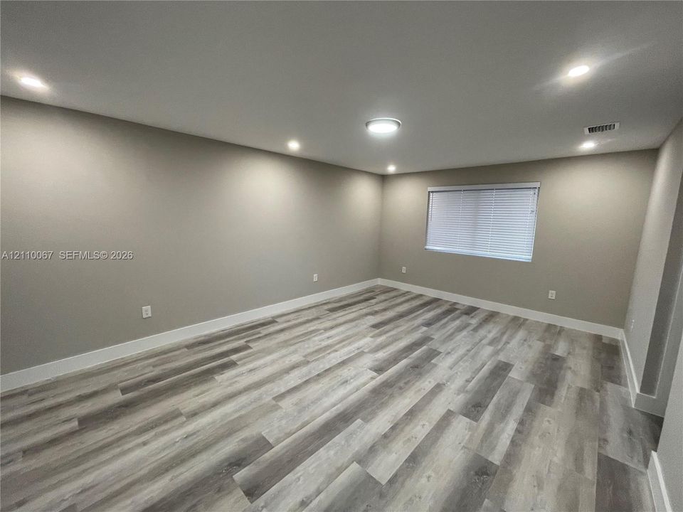 Neutral-toned room featuring wood-finish flooring, recessed lighting, and a window with horizontal blinds
