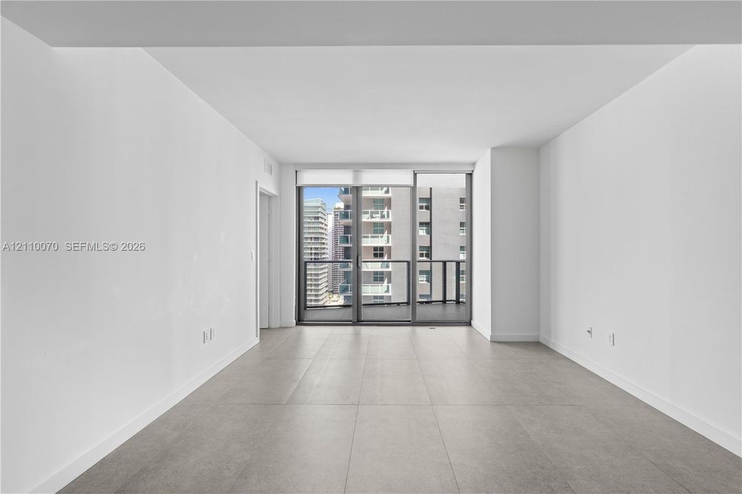 Open-concept interior featuring oversized tile flooring, high ceilings, floor-to-ceiling glass sliding doors, and a private balcony