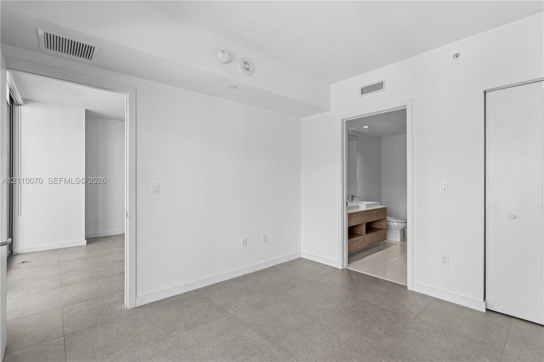 Large-format neutral floor tiling, clean white wall finishes, and a reach-in closet with sliding doors