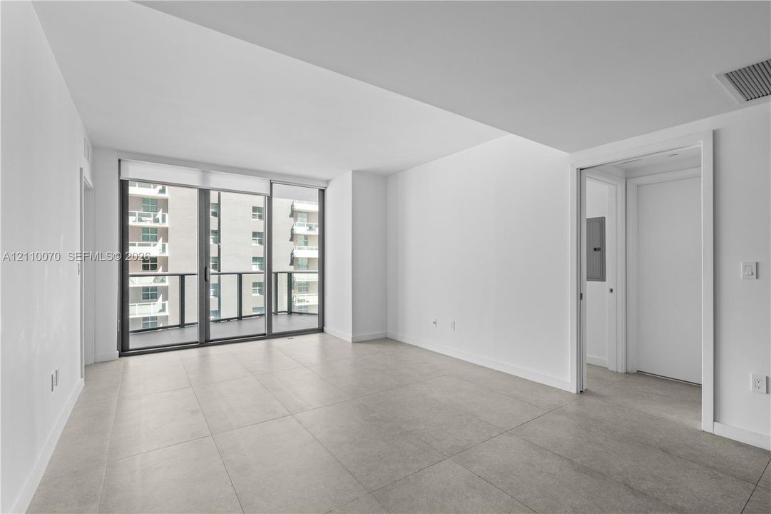 Floor-to-ceiling glass sliding doors, private balcony, neutral large-format tile flooring, and crisp white wall finishes