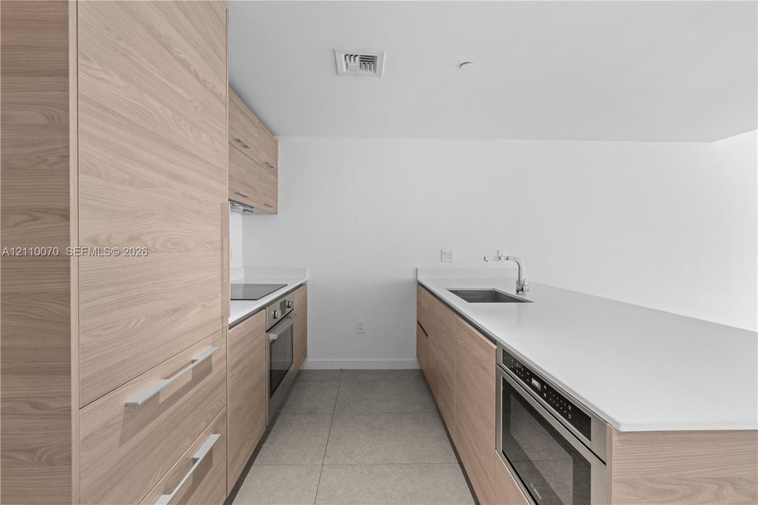 Kitchen featuring wood-finish cabinetry, white solid-surface countertops, a stainless steel undermount sink with a gooseneck faucet, a built-in microwave, and tile flooring