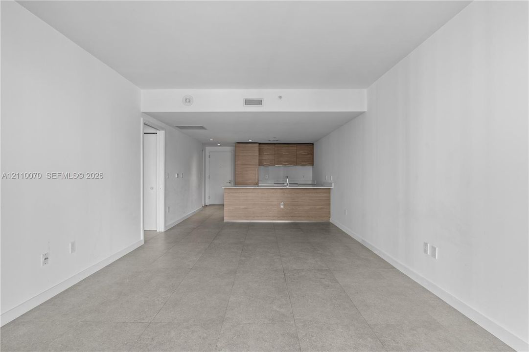 Open-concept interior featuring large-format tile flooring, wood-finish cabinetry, and solid-surface countertops