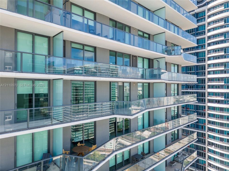 High-rise exterior featuring stepped balconies with glass railings and floor-to-ceiling sliding glass doors