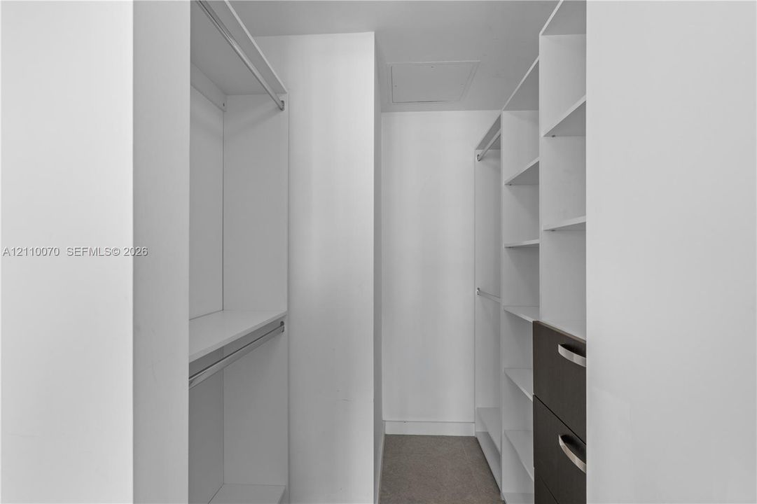 Walk-in closet featuring white built-in shelving, integrated hanging rods, and dark-toned drawers with metallic hardware