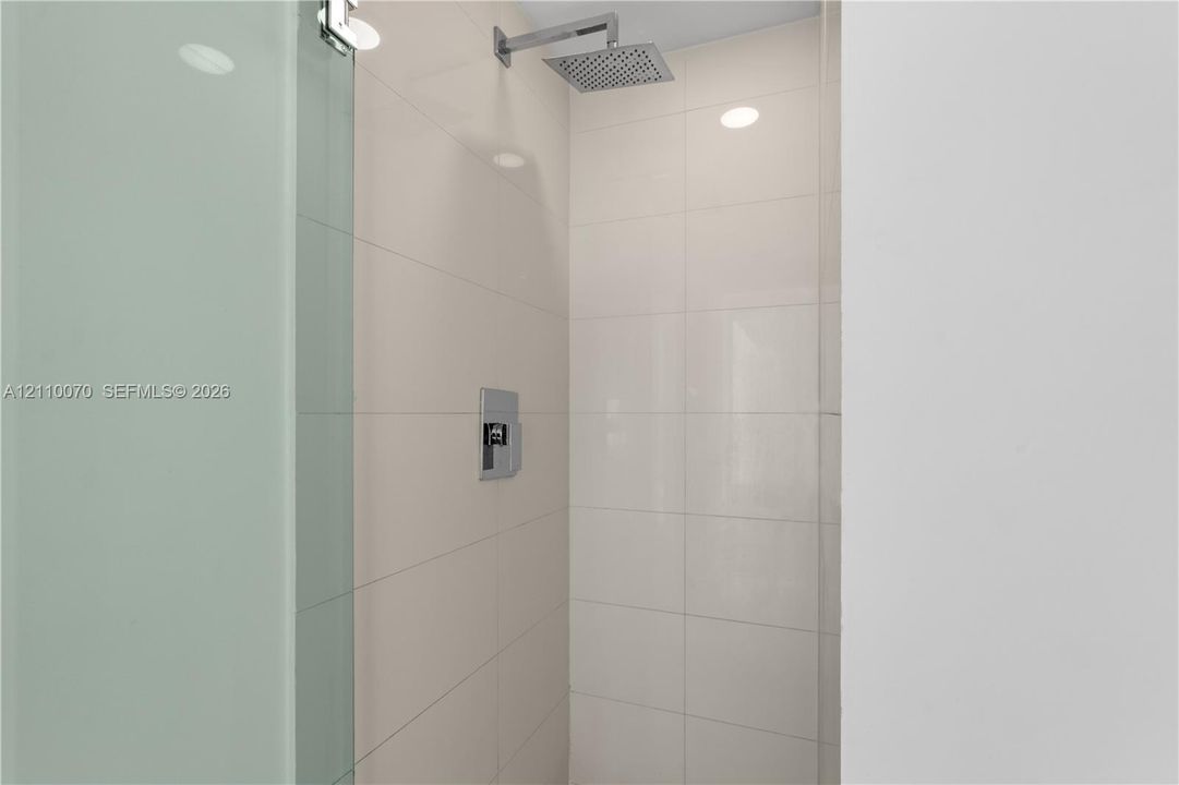 Walk-in shower featuring large-format ceramic tile, glass enclosure, and a chrome overhead rainfall showerhead