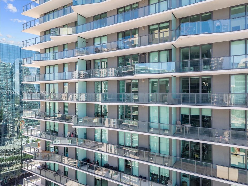 High-rise exterior featuring stepped balconies, floor-to-ceiling glass paneling, integrated glass railing systems, and concrete structural elements
