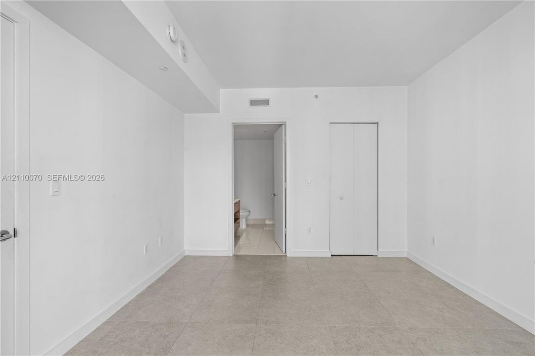 Neutral-toned room featuring large-format tile flooring, smooth ceiling finishes, and a double-door closet