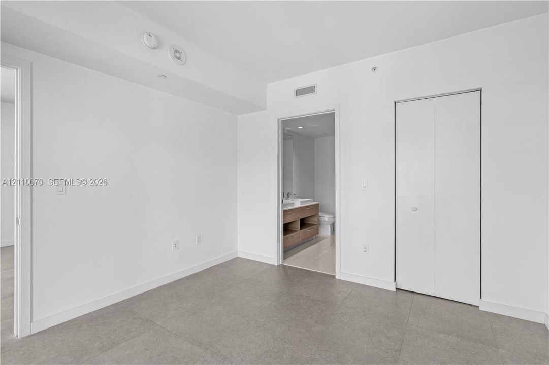Neutral-toned floor tiling, bi-fold closet doors, and smooth, high-contrast wall finishes
