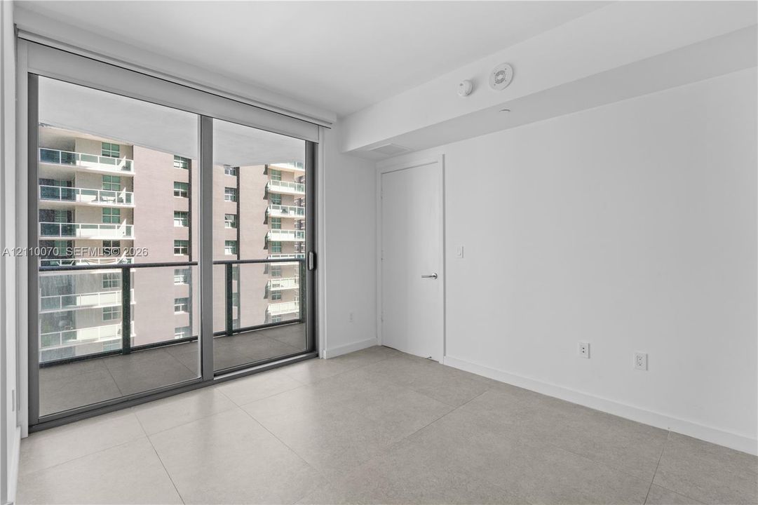 Floor-to-ceiling sliding glass doors, private balcony with metal railing, large-format tile flooring, and minimalist interior aesthetic