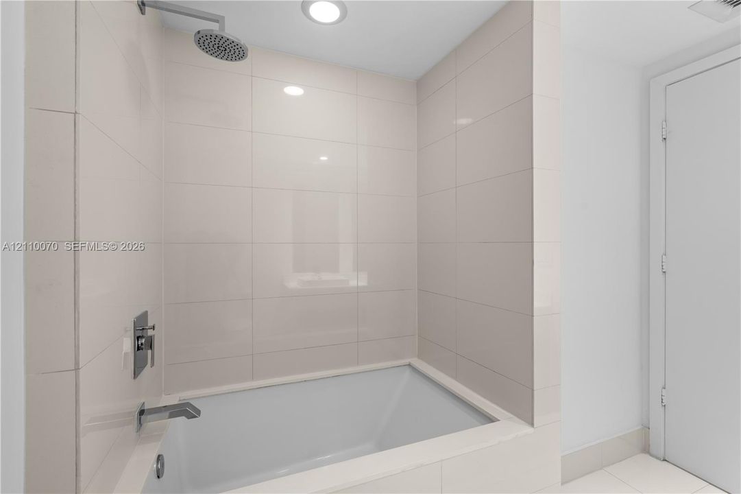 Deep-soaking bathtub with rectangular integrated surround, wall-mounted chrome rainfall showerhead, and polished chrome hardware