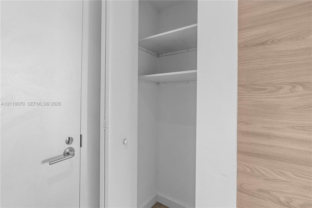 Built-in closet featuring white shelving, a solid white door with a satin-nickel lever handle, and a wood-finish wall panel