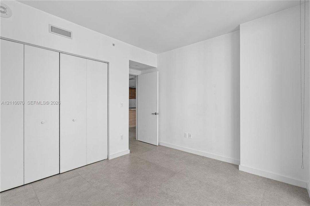 Room featuring large-format tile flooring, white walls, and built-in closet with four-panel folding doors