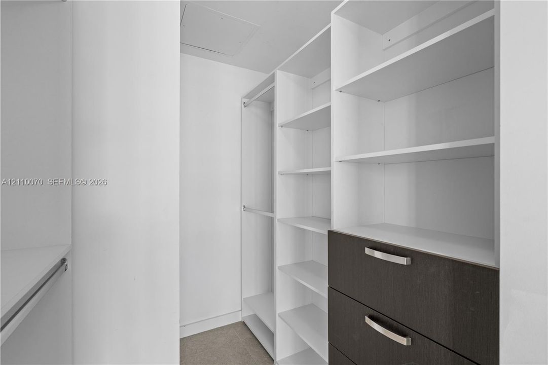 Walk-in closet featuring white built-in shelving, hanging rods, and integrated cabinetry with dark-finish drawers and metallic hardware