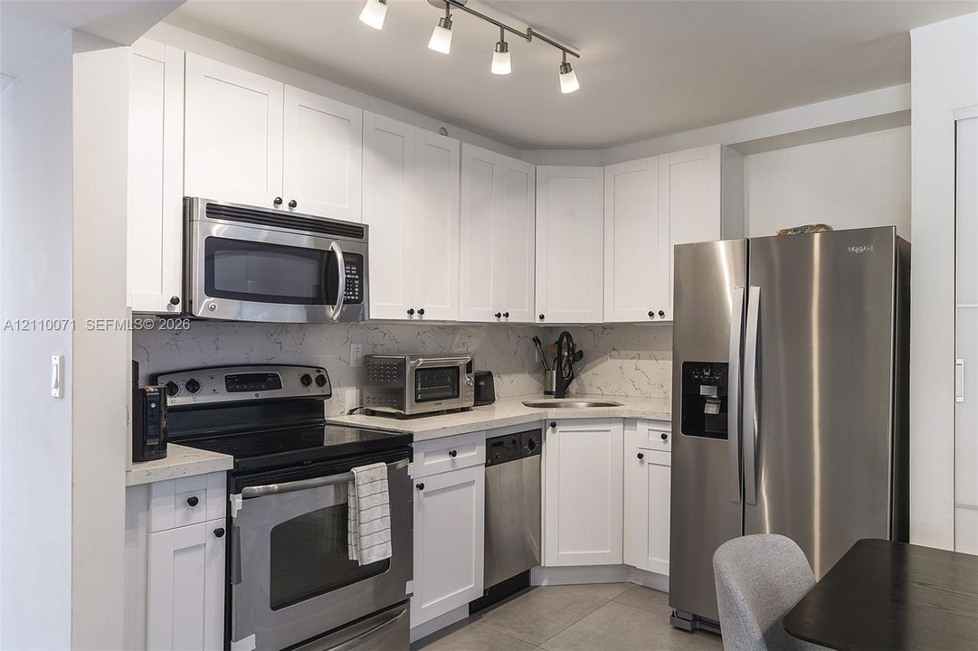 Kitchen featuring white shaker-style cabinetry, stainless steel appliances, quartz countertops with matching backsplash, and ceiling-mounted track lighting