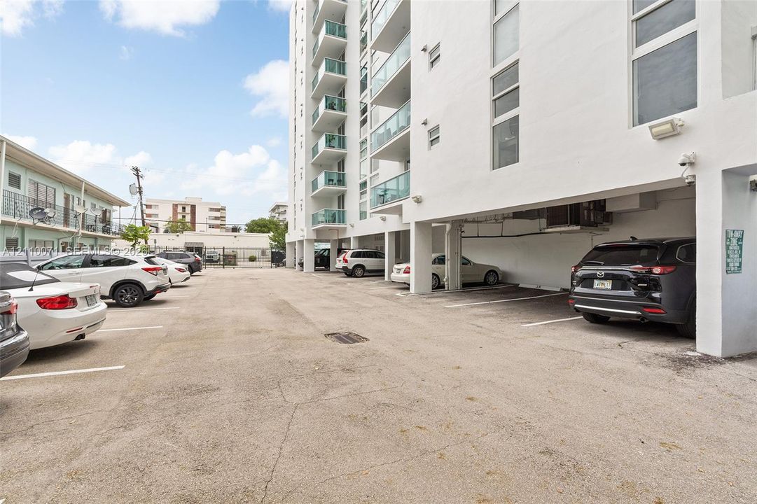 Asphalt surface parking area featuring assigned spaces and covered parking beneath the building structure