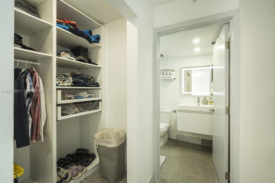 Custom built-in closet shelving featuring integrated drawers and hanging rods, accompanied by a bathroom with a wall-mounted floating vanity, LED-backlit mirror, and tile flooring