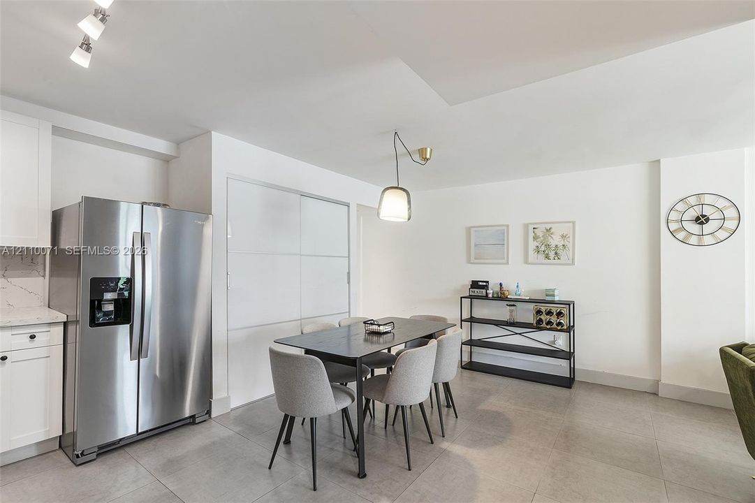 Stainless steel side-by-side refrigerator, white shaker-style cabinetry, matte tile flooring, contemporary pendant lighting, and built-in closet with sliding panels