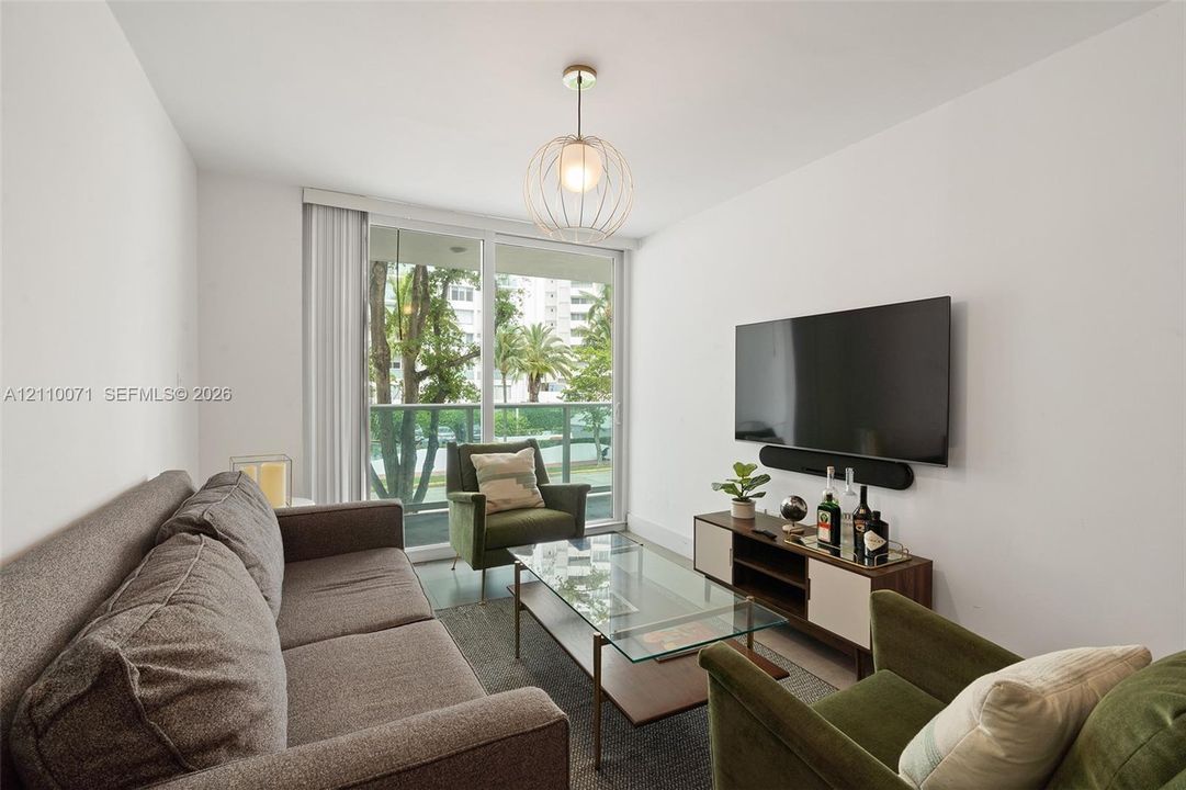 Living area featuring large-format sliding glass doors, neutral walls, and a modern spherical metal pendant light