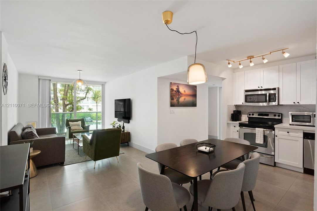Open-concept interior featuring large-format tile flooring, white cabinetry, stainless steel appliances, and a glass sliding door providing outdoor access