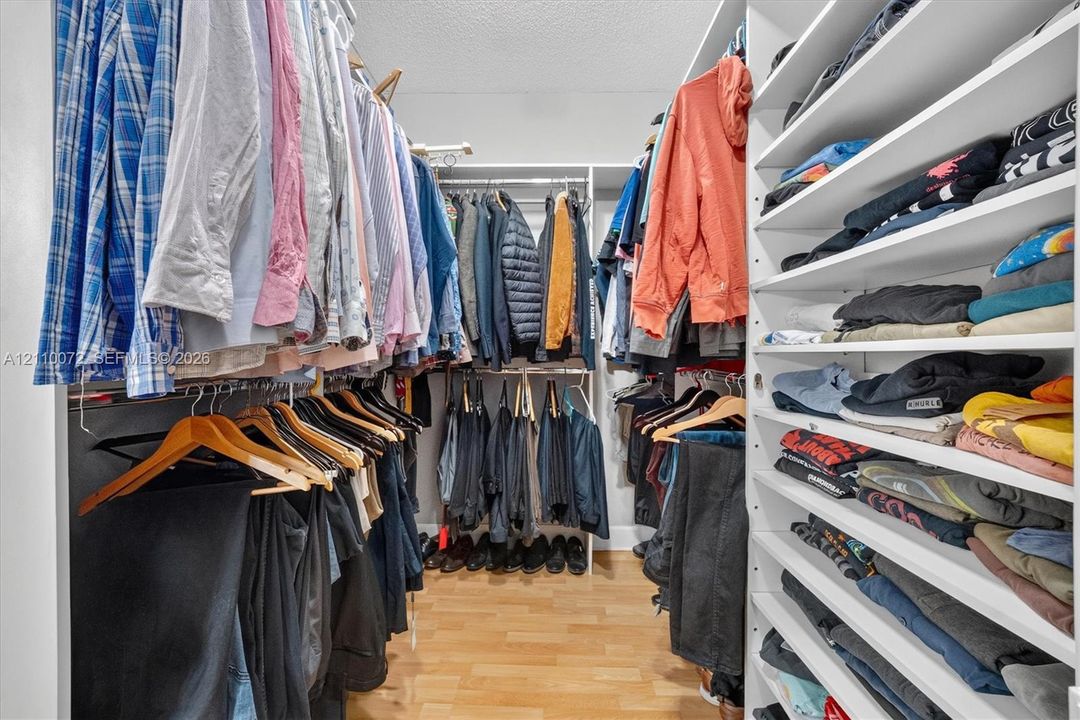 Walk-in closet featuring extensive built-in white shelving, multiple hanging rods, and wood-finish flooring