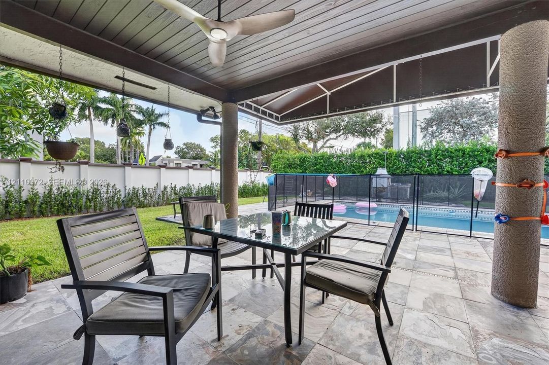 Covered outdoor patio featuring slate tile flooring, a wood-paneled ceiling, a ceiling fan, and structural columns