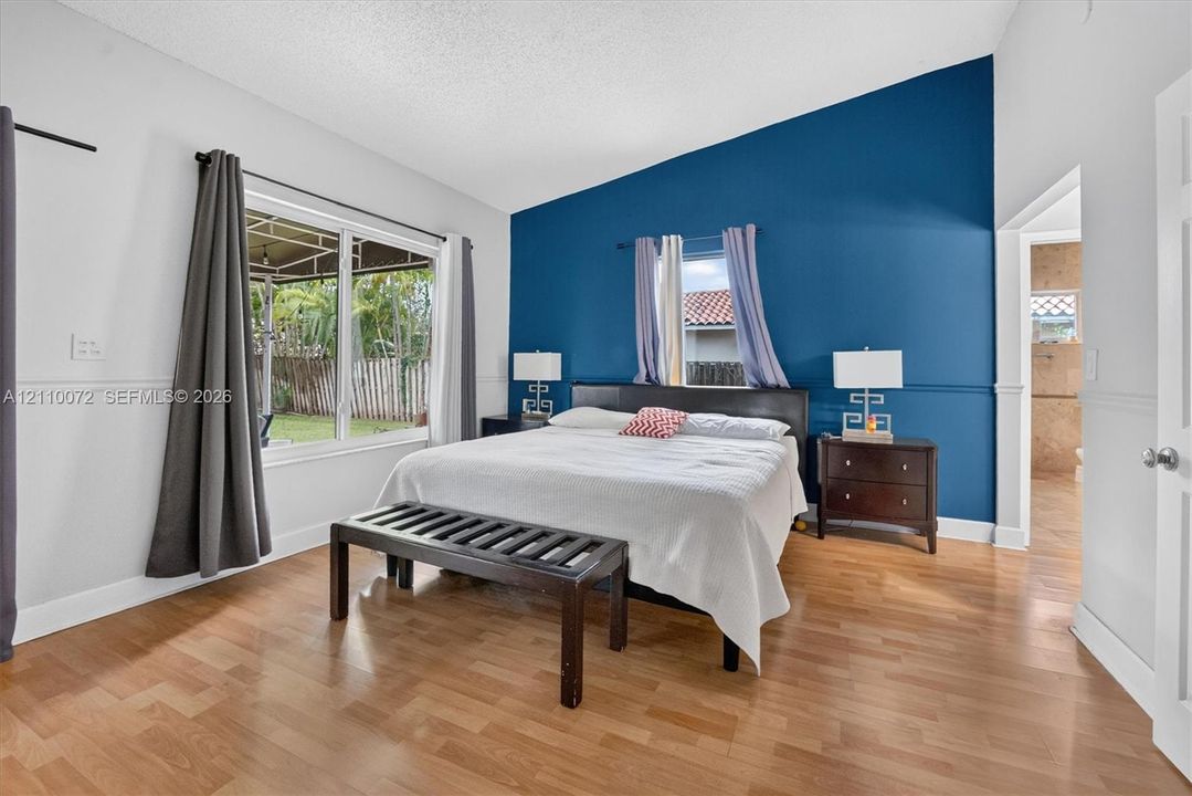 Vaulted ceiling, wood-finish flooring, accent wall, and large windows with outdoor exposure