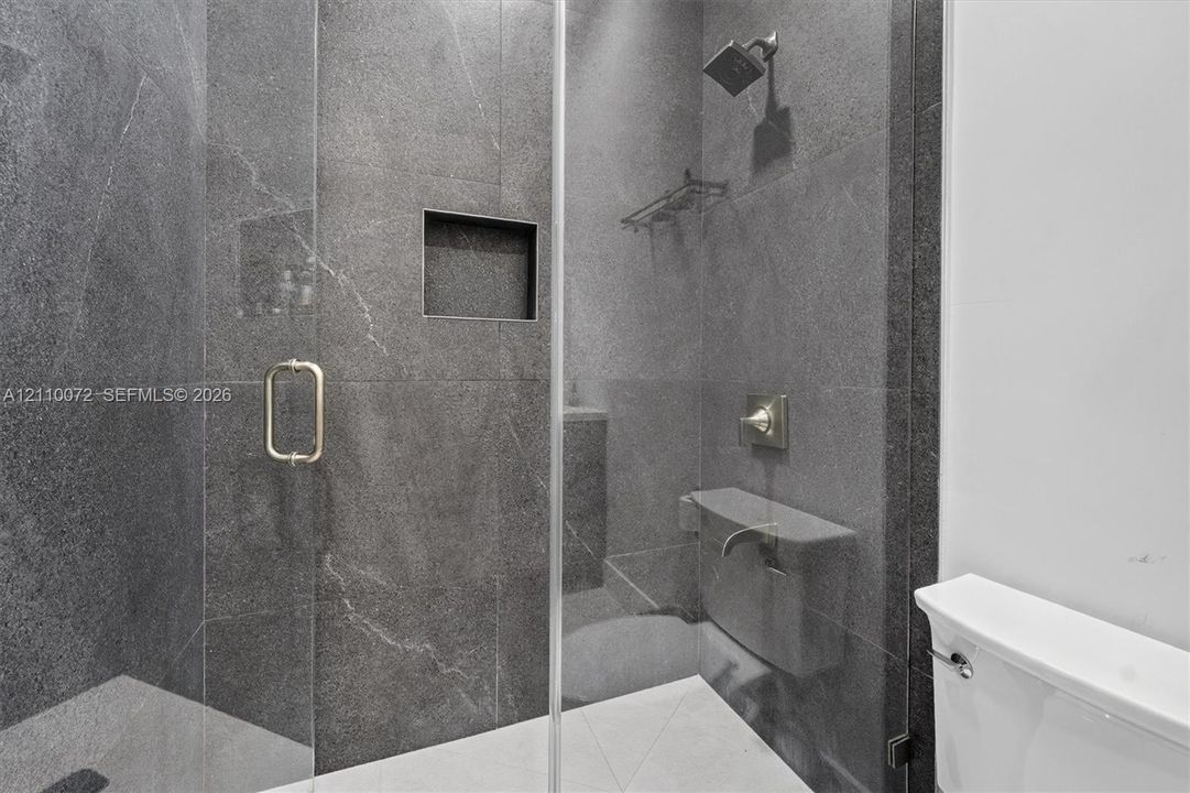 Walk-in shower featuring floor-to-ceiling stone-finish tile, frameless glass door, built-in wall niche, brushed metallic fixtures, and a stationary shower head