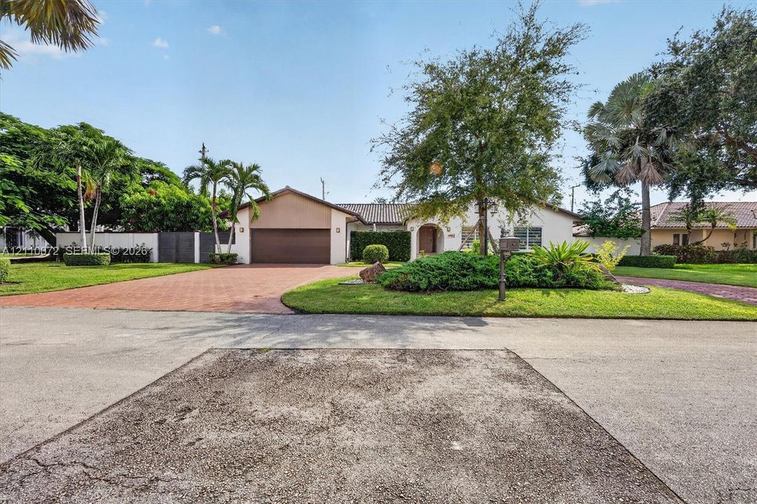 Single-story residence featuring a tile roof, brick-paver driveway, attached multi-car garage, and established landscaping