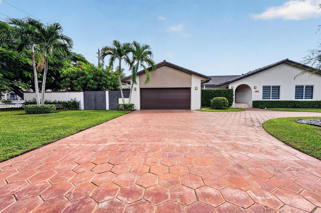Single-story residence featuring a hexagonal paver driveway, an attached garage, and manicured landscaping with palm trees