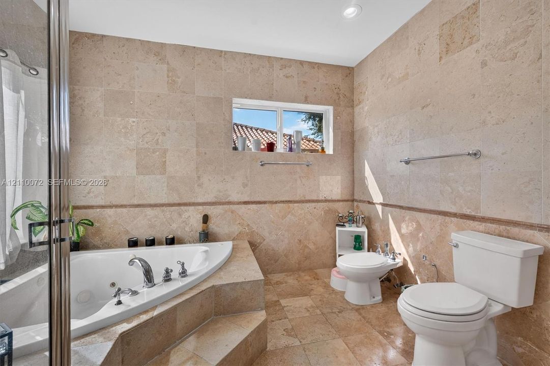 Bathroom featuring floor-to-ceiling stone-tile wall finishes, a recessed jetted soaking tub with a tiled surround, and integrated tile flooring