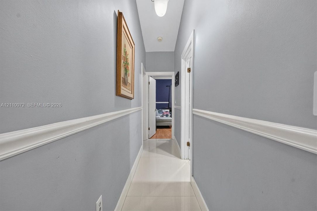 Hallway featuring light-toned tile flooring, chair rail molding, and crisp white door casings