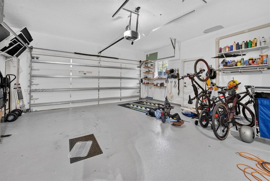 Attached two-car garage featuring a sectional metal door, epoxy-coated flooring, built-in shelving units, and a dedicated service door