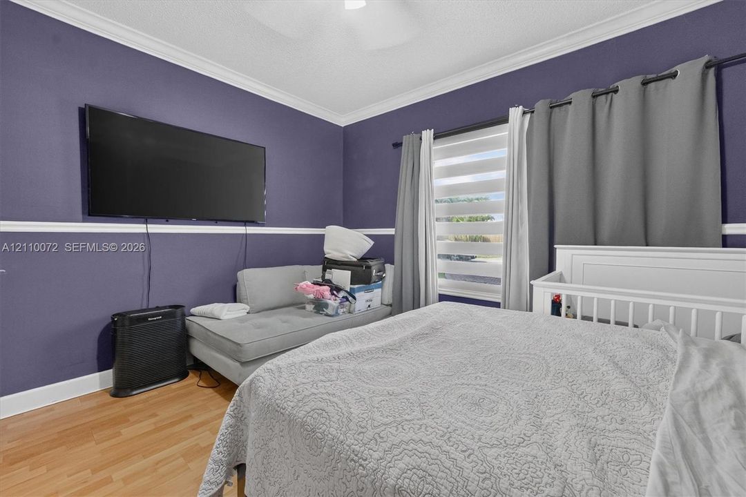 Room featuring wood-finish flooring, white crown molding, crisp white chair rail, and horizontal window blinds
