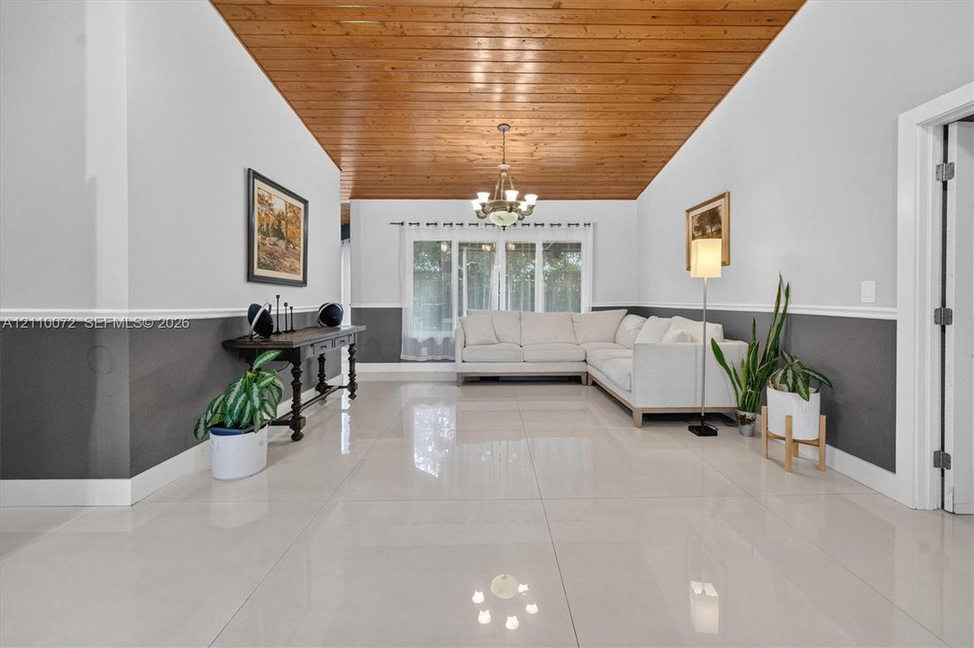 Vaulted wood-plank ceiling, large-format tile flooring, multi-pane window, and decorative chair rail molding