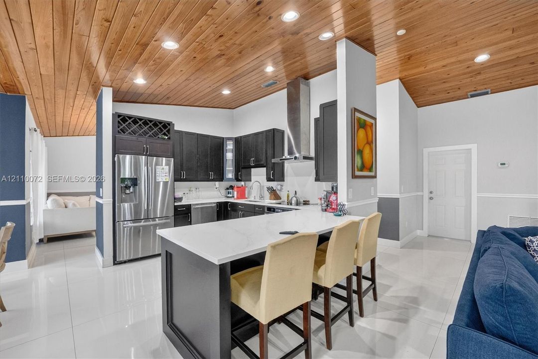 Kitchen featuring vaulted wood-plank ceilings, a central island with a solid-surface countertop, dark-toned cabinetry, stainless steel appliances, and polished tile flooring