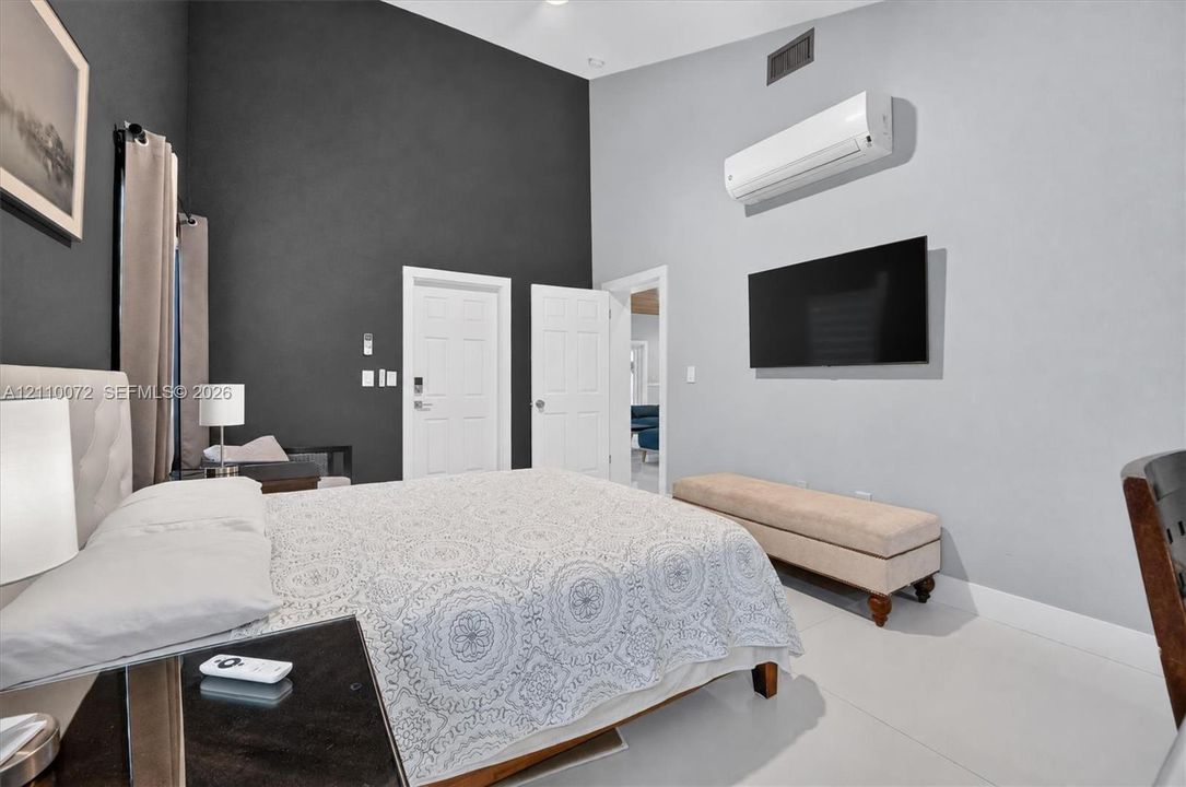 High-ceiling interior featuring a dual-tone accent wall, wall-mounted climate control unit, and crisp light-colored flooring