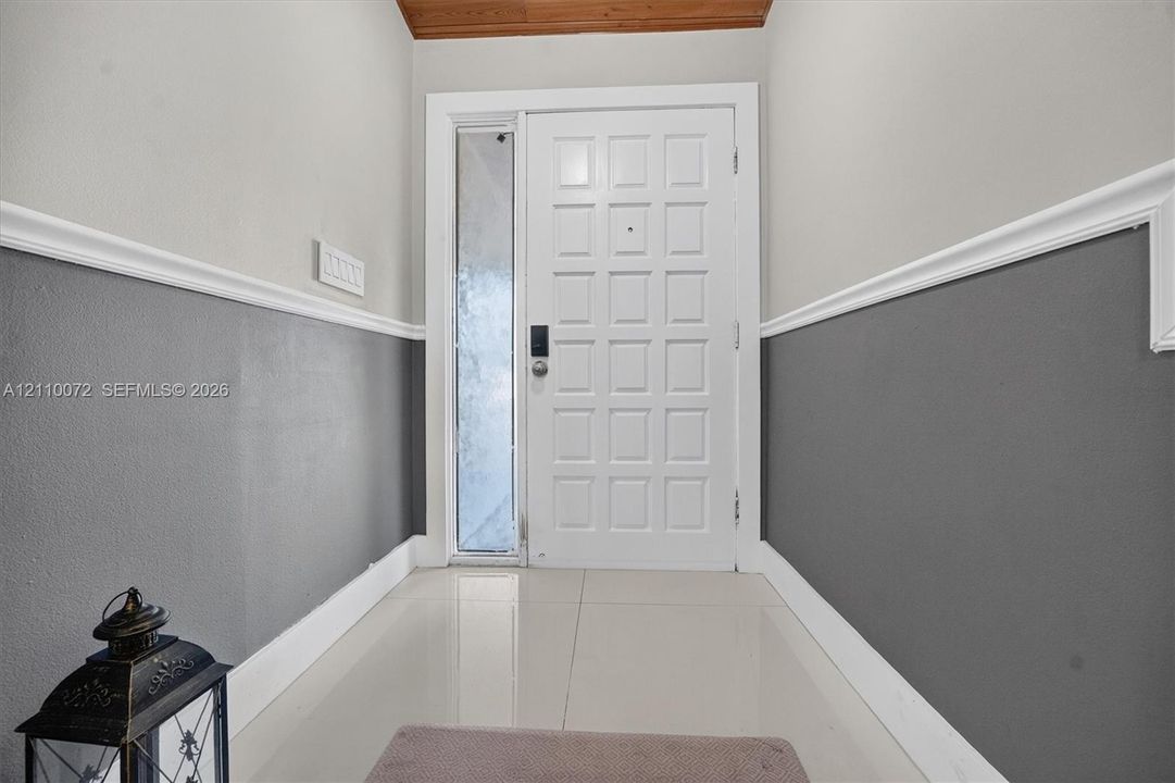 Entryway featuring a grid-patterned door with a vertical glass side panel, two-tone wall finish with decorative chair rail molding, and large-format tile flooring