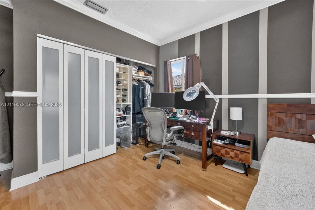 Room featuring wood-finish flooring, crown molding, chair rail trim, and a built-in closet system with frosted glass panels